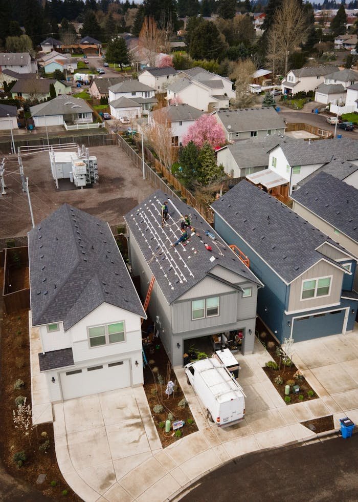 Aerial View of a House with Crew Installing Solar Panels on the Roof